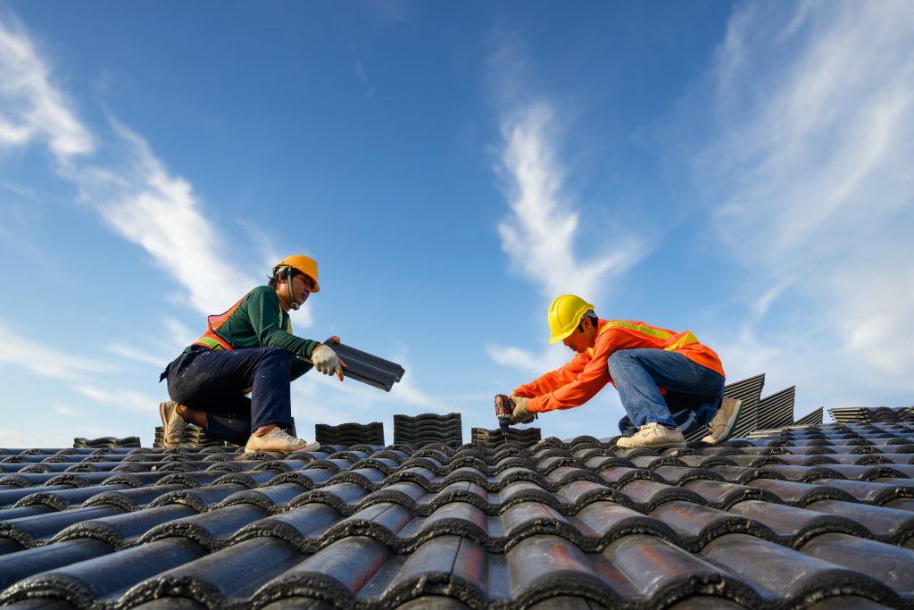 Asian male roof installer Asian construction workers on the roof Work using a drill bit to fix ceramic or cement roofing screws on the construction site.