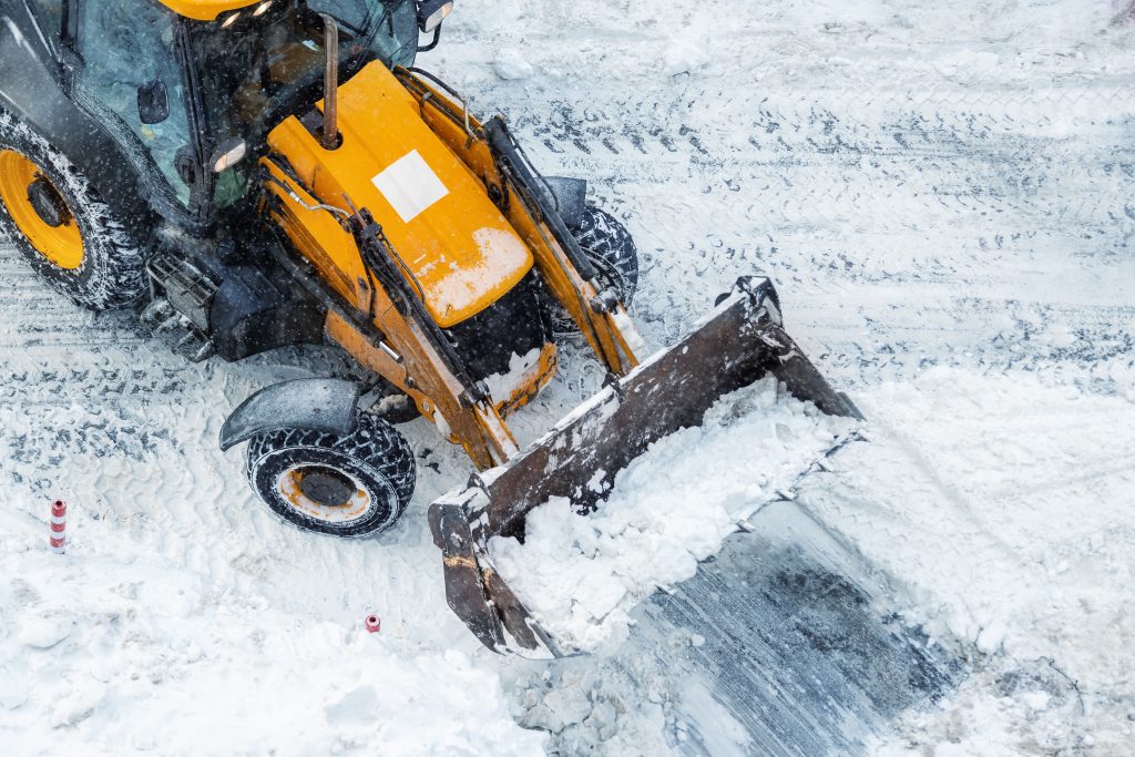 Tractor loader machine uploading dirty snow into dump truck. Cleaning city street, removing snow and ice after heavy snowfalls and blizzard. Snowplow outdoors clean pavement sidewalk road driveway