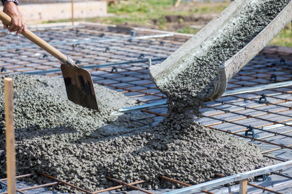 Worker takes concrete from a mixer tray with a shovel.