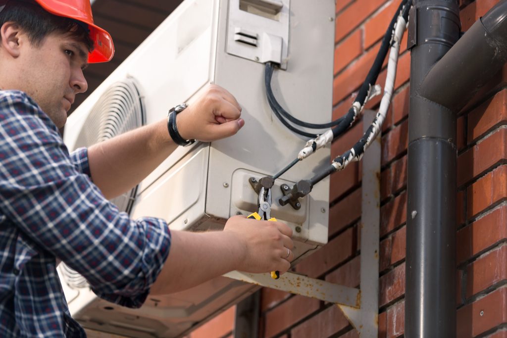 Closeup image of male repairman connecting air conditioner pipes and tubes